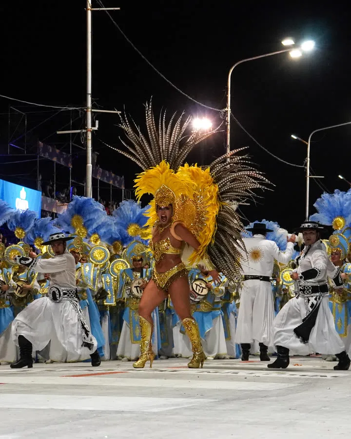 Comparsa de carnaval con plumas celestes y doradas, de noche