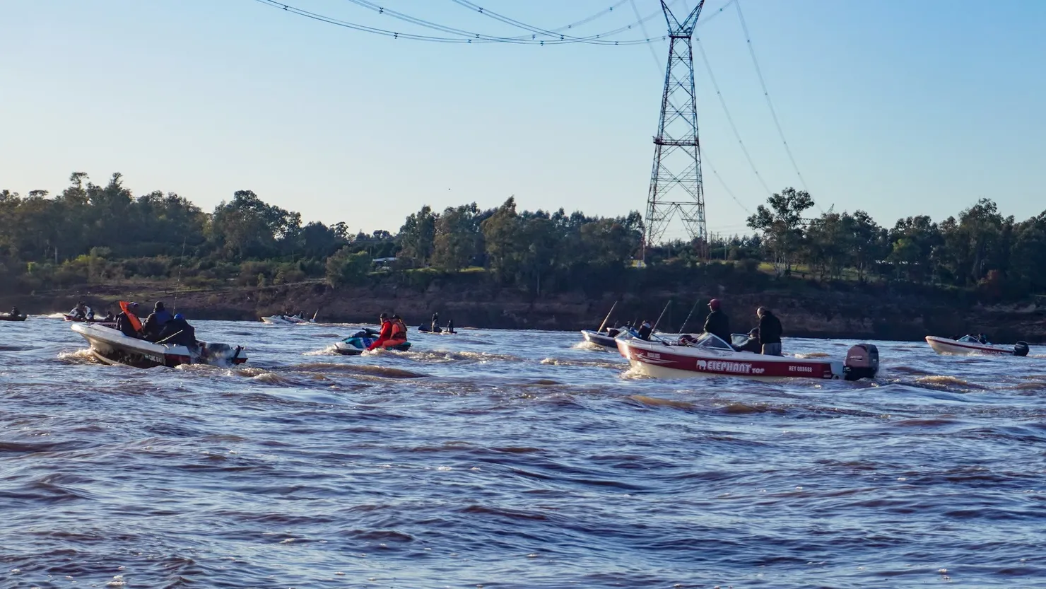 Lanchas y kayaks sobre el río, con una torre de alta tensión de fondo